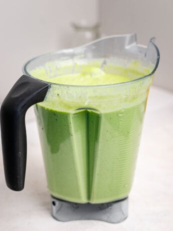 Creamy kids green smoothie made with spinach, bananas, and frozen fruit blended until smooth in a high-speed blender pitcher, ready to be poured into homemade smoothie pouches.