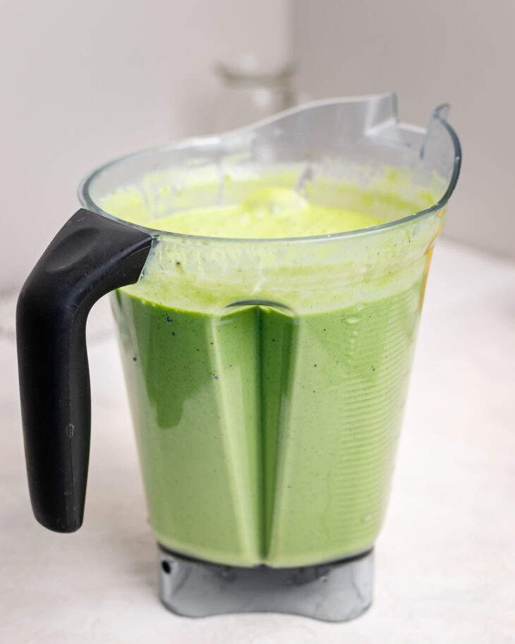 Creamy kids green smoothie made with spinach, bananas, and frozen fruit blended until smooth in a high-speed blender pitcher, ready to be poured into homemade smoothie pouches.