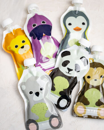 Reusable animal-shaped smoothie pouches filled with homemade kids green smoothie made with spinach and fruit, ready for freezer-friendly snacks.