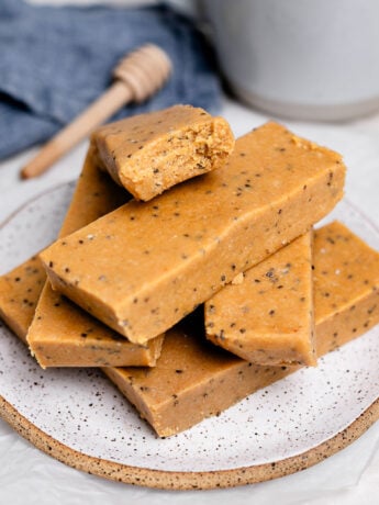 Stack of homemade copycat Perfect Bars on a plate, showing soft, chewy peanut butter almond flour texture with chia seeds, with one bar bitten to reveal the inside, a no-bake healthy protein snack.