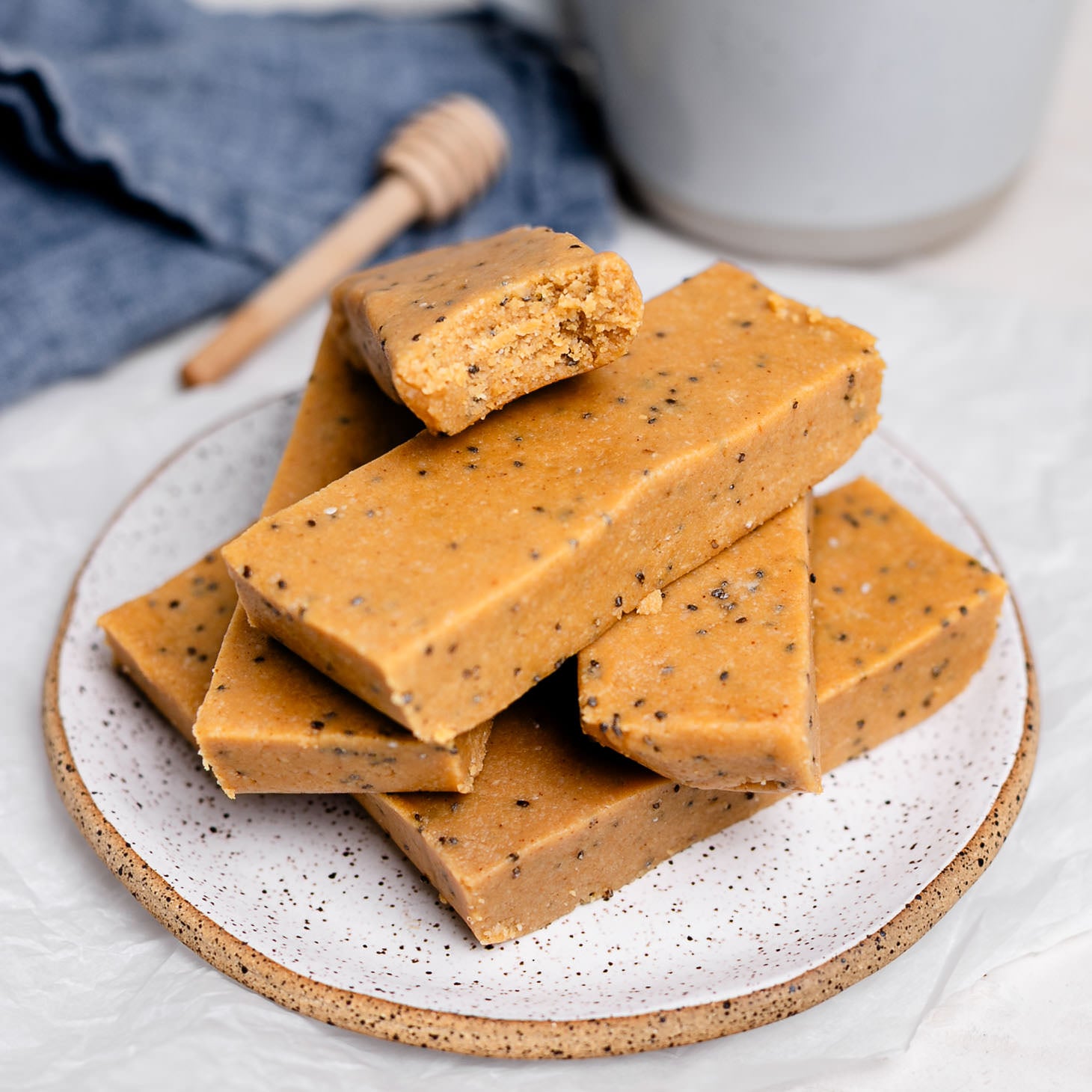 Stack of homemade copycat Perfect Bars on a plate, showing soft, chewy peanut butter almond flour texture with chia seeds, with one bar bitten to reveal the inside, a no-bake healthy protein snack.