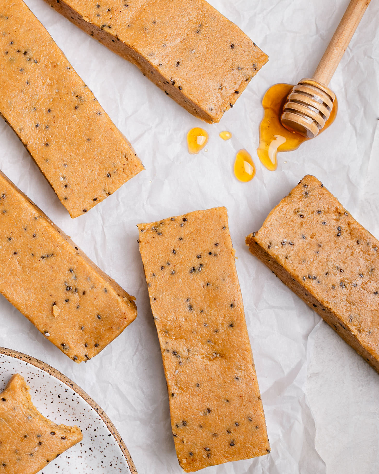 Overhead view of homemade copycat Perfect Bars made with peanut butter and almond flour, speckled with chia seeds, arranged on parchment paper with a honey dipper and drizzle, showing soft no-bake protein bars.