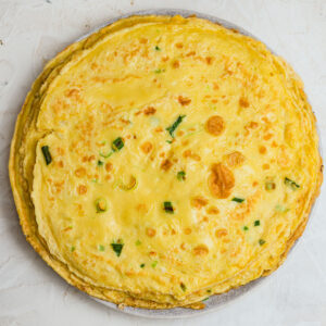 Stack of homemade Chinese Egg Pancakes (鸡蛋饼) on a plate, featuring golden brown spots, tender edges, and fresh scallions throughout. These savory Chinese crepe-style pancakes are soft, chewy, and a traditional comfort breakfast made with eggs, flour, and scallions.