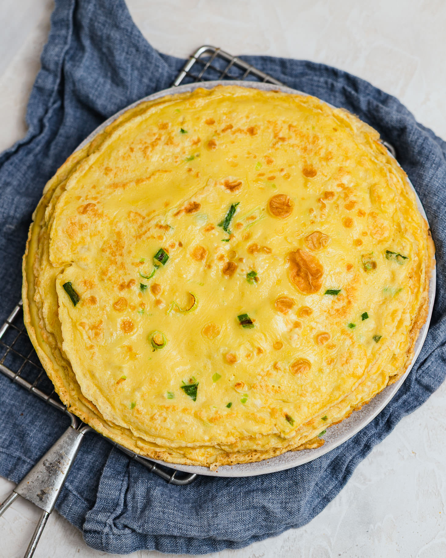 A plate on a cooling rack holding a few Chinese egg pancakes 鸡蛋饼. there are pieces of scallions in the ji dan bing, the edge of them appear to be crispy.