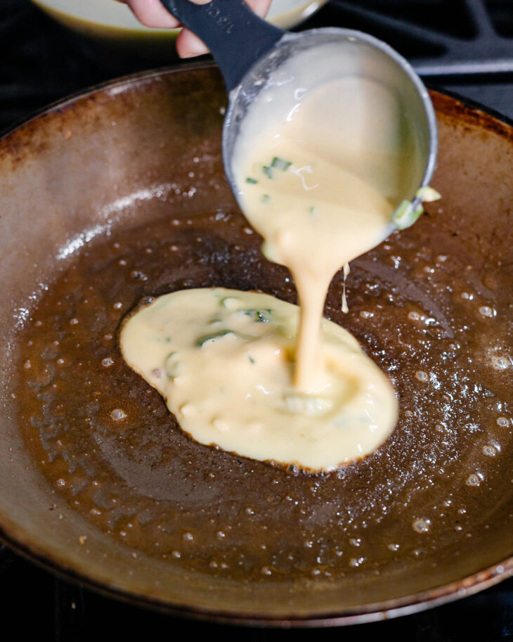 Grease the pan and once it is warm, a hand is adding the batter.