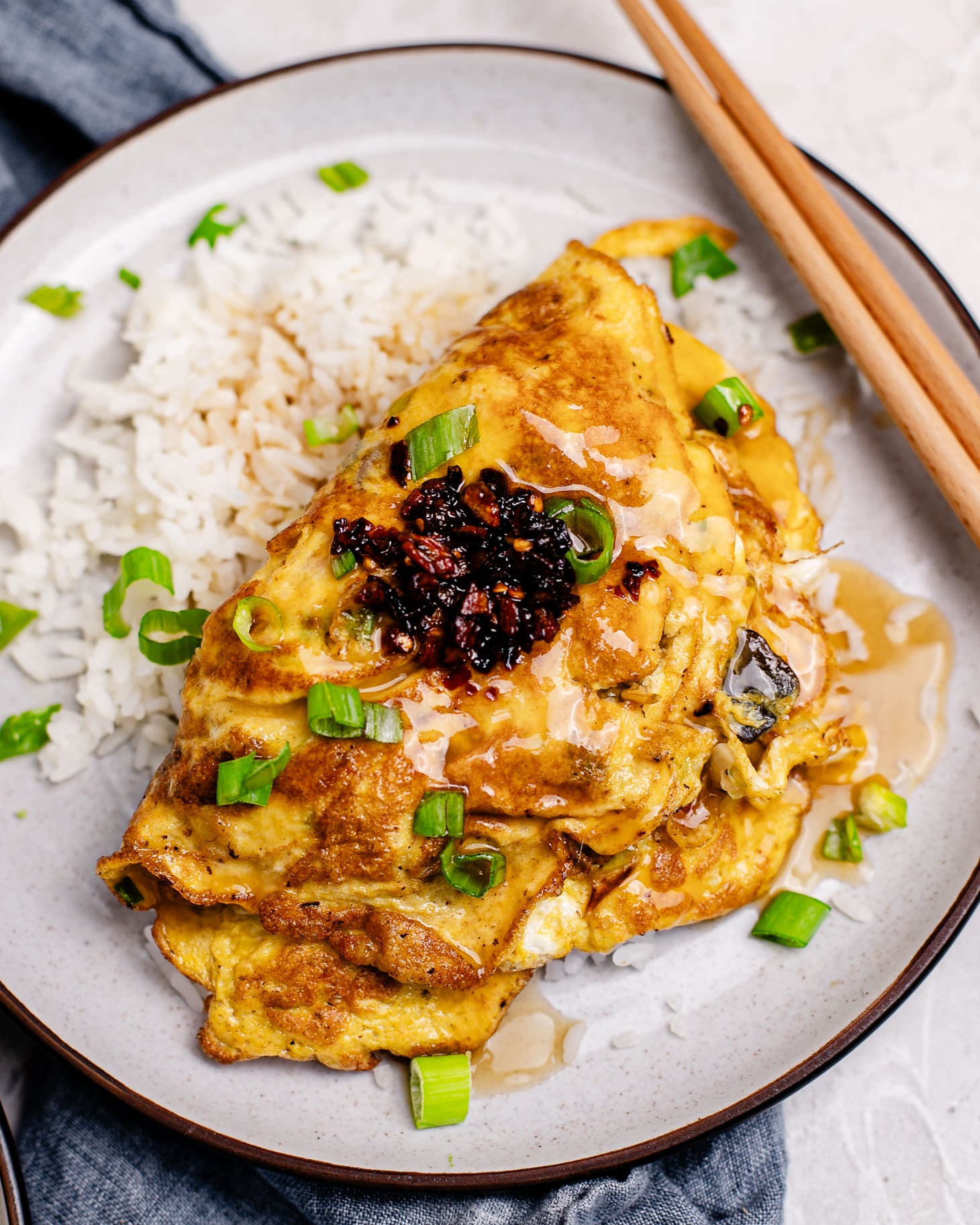 Homemade Shrimp Egg Foo Young omelet served over steamed white rice, topped with savory gravy, green onions, and chili crisp.