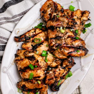 Asian grilled chicken thighs marinated with coconut aminos, garlic, honey, and Shaoxing wine, grilled until caramelized and juicy, topped with green onions on a white plate