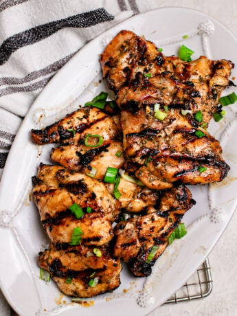 Asian grilled chicken thighs marinated with coconut aminos, garlic, honey, and Shaoxing wine, grilled until caramelized and juicy, topped with green onions on a white plate