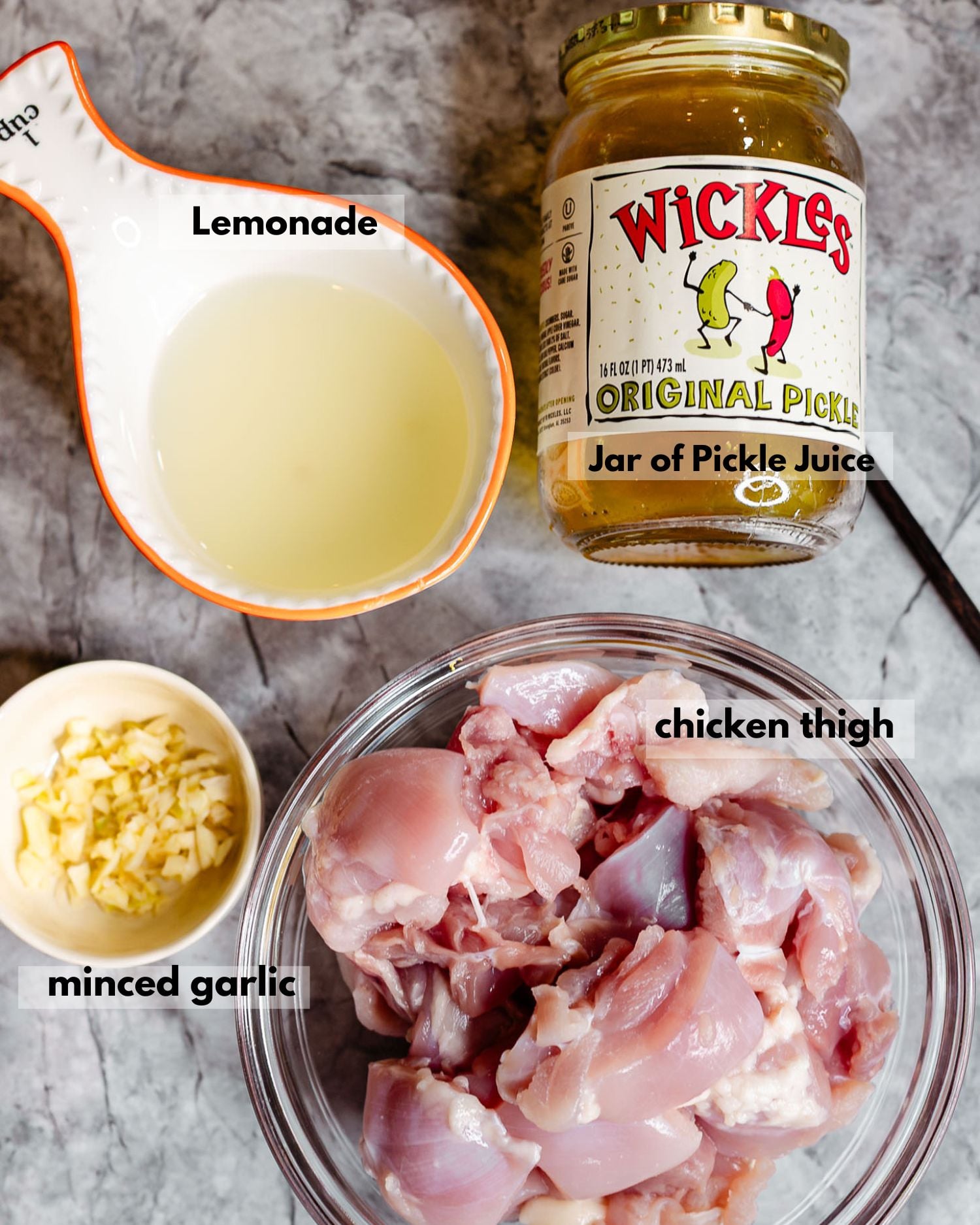 Ingredients for lemonade pickle brined chicken skewers displayed on a countertop, including chicken thighs, a jar of pickle juice, lemonade, and minced garlic. The simple four-ingredient marinade creates juicy, flavorful grilled chicken perfect for summer cookouts and backyard barbecues.