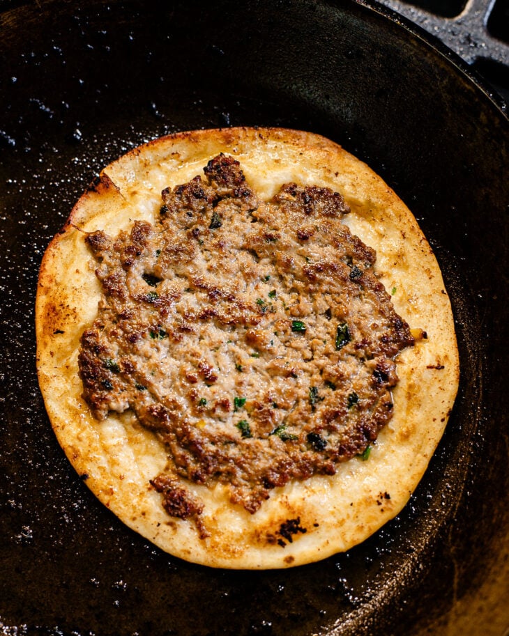 A crispy brown tortilla with browned cooked pork dumpling filling on top, on a greased skillet.