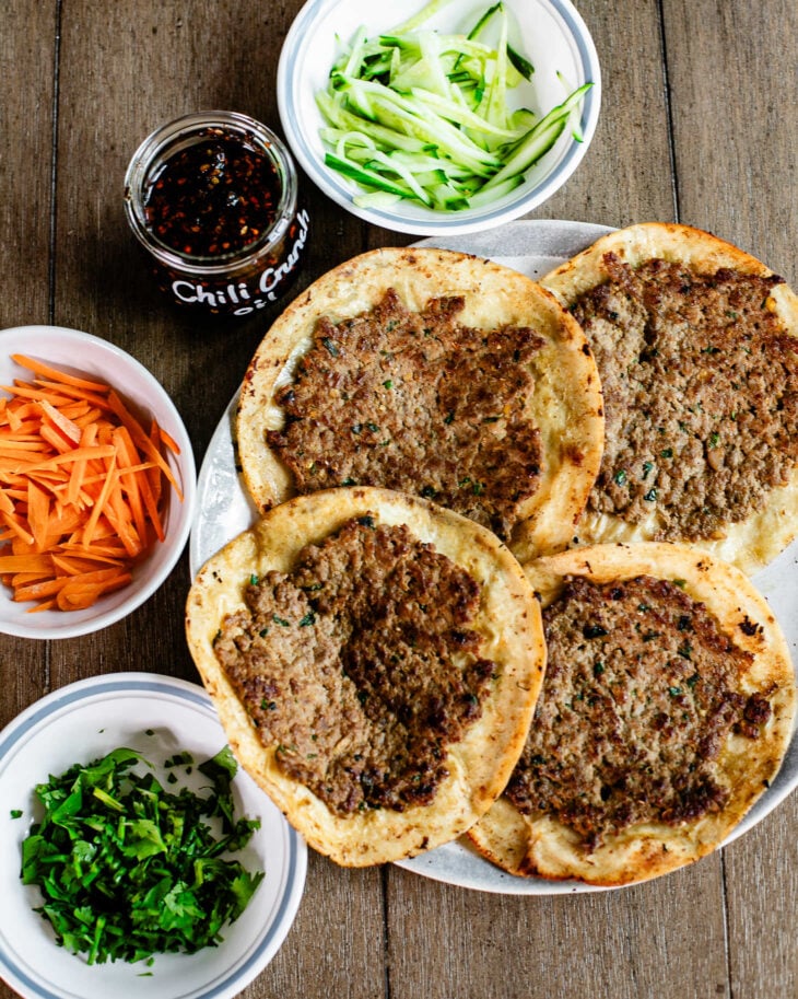 4 pieces of cooked dumpling tacos with sliced cucumbers, carrots, cilantro and chili crisp on the side, ready to be used as toppings for the tacos.
