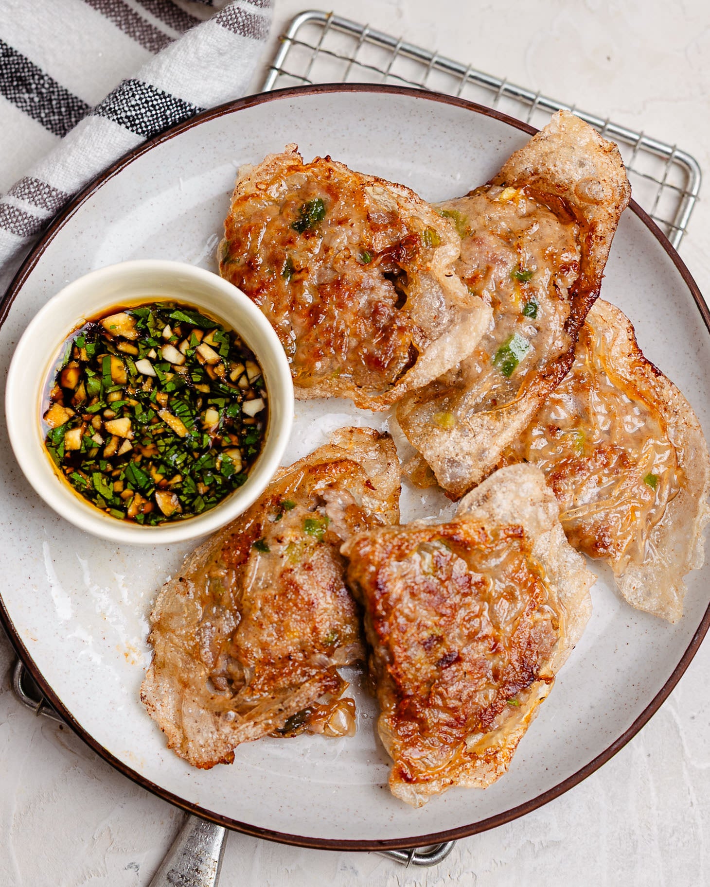 Plate of crispy rice paper dumplings filled with juicy pork and green onions, pan-fried until golden brown and served with a savory dipping sauce made with soy sauce, garlic, and fresh herbs. The dumplings have crunchy, blistered edges and are arranged on a white ceramic plate for an easy homemade appetizer or weeknight dinner.
