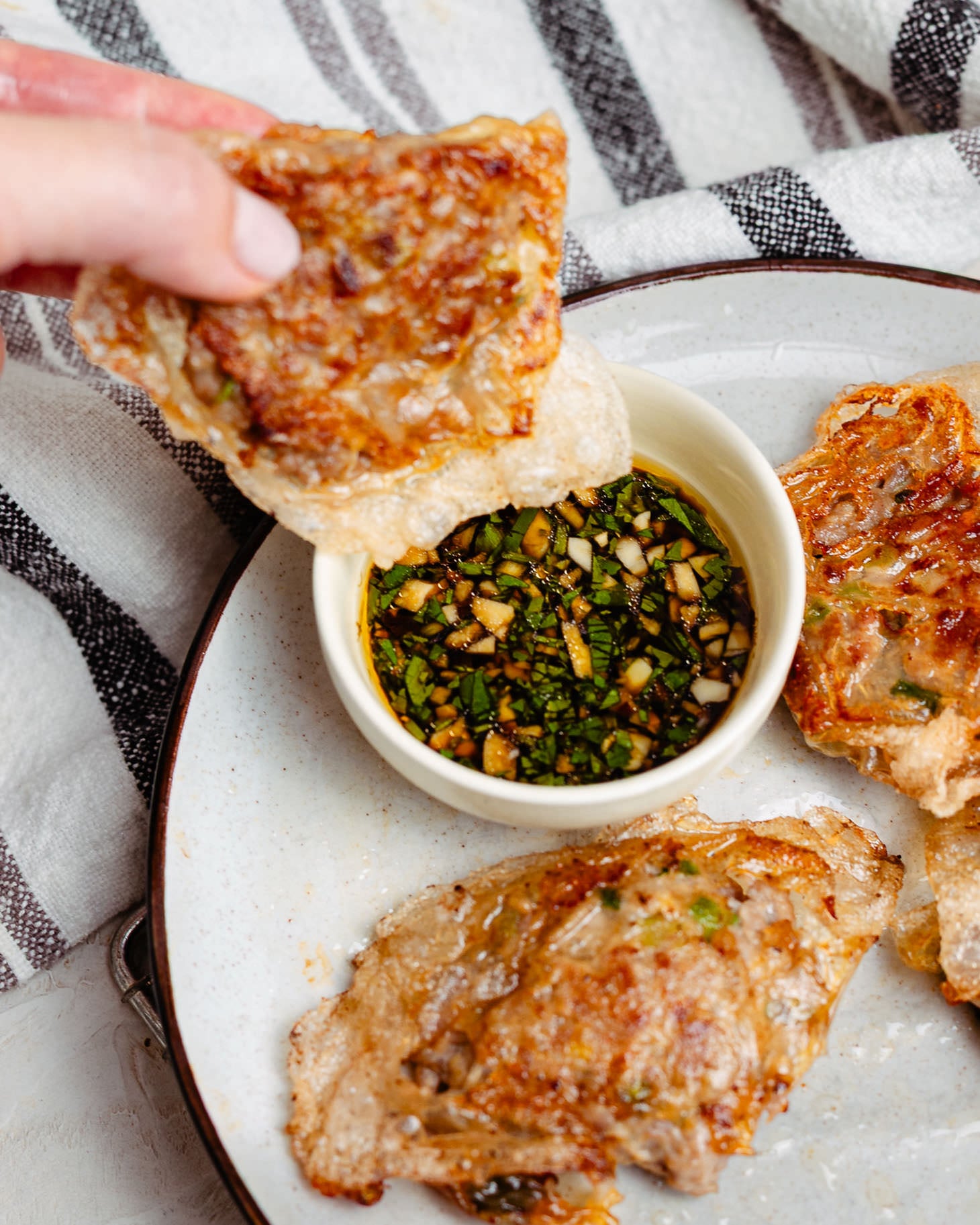 Hand dipping a crispy homemade Chinese dumpling into a garlic cilantro dumpling sauce made with black vinegar, soy sauce, and sesame oil.