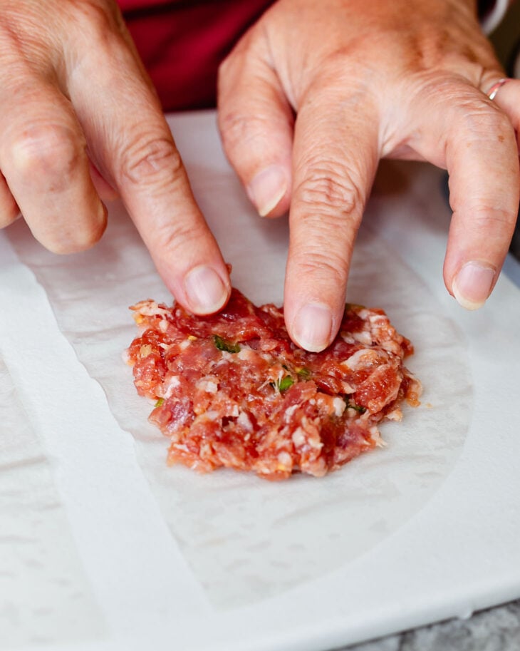 My fingers pressing down dumpling filling on top of a piece of rice paper to make rice paper wrapped dumplings.