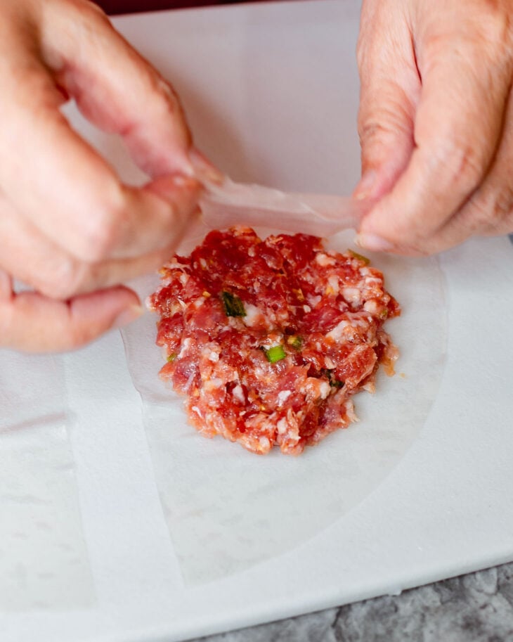 Two hands gently press and spread the filling into an even layer while leaving a border around the edges.