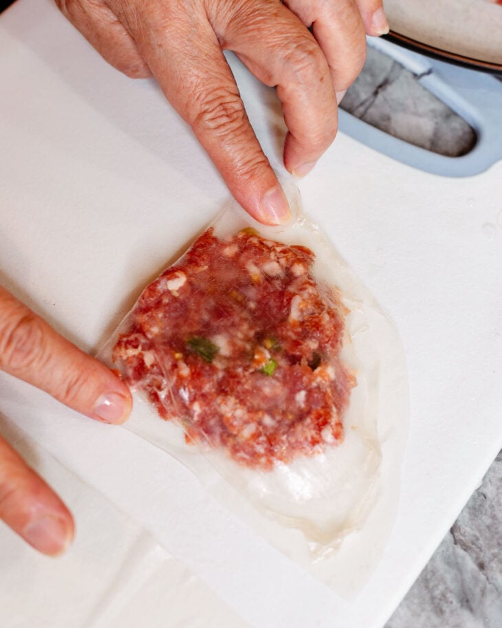 Two hands gently using the second finger to fold the rice paper over into a half moon and press the edges together.