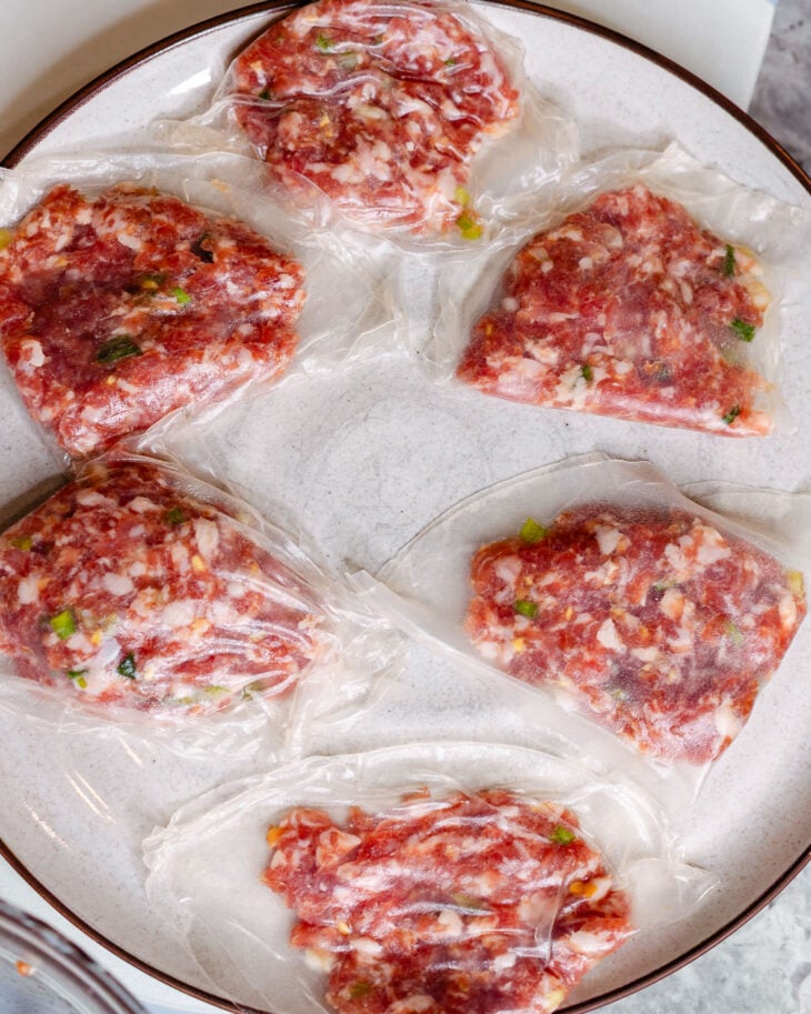 6 uncooked rice paper dumplings are assembled and placed on a plate.