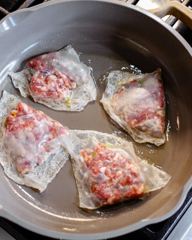 A non-stick pan with a layer of cooking oil heated up. There are 4 uncooked rice paper dumplings placed on the pan.