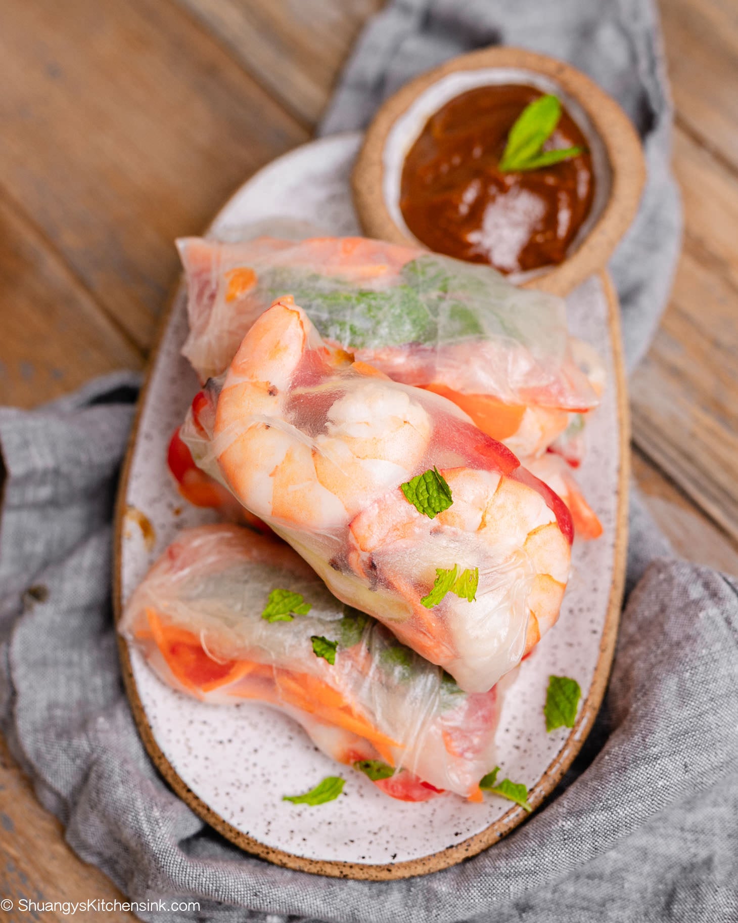 Fresh homemade shrimp spring rolls filled with juicy shrimp, cucumbers, carrots, red bell peppers, and mint, served with creamy peanut dipping sauce on a ceramic platter.