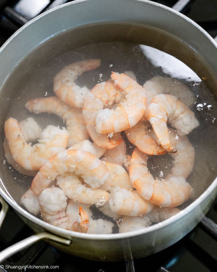 Shrimp boiling in water in a silver pot over the stove.