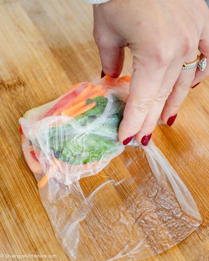 A hand holding the bottom over the filling and roll tightly until sealed.