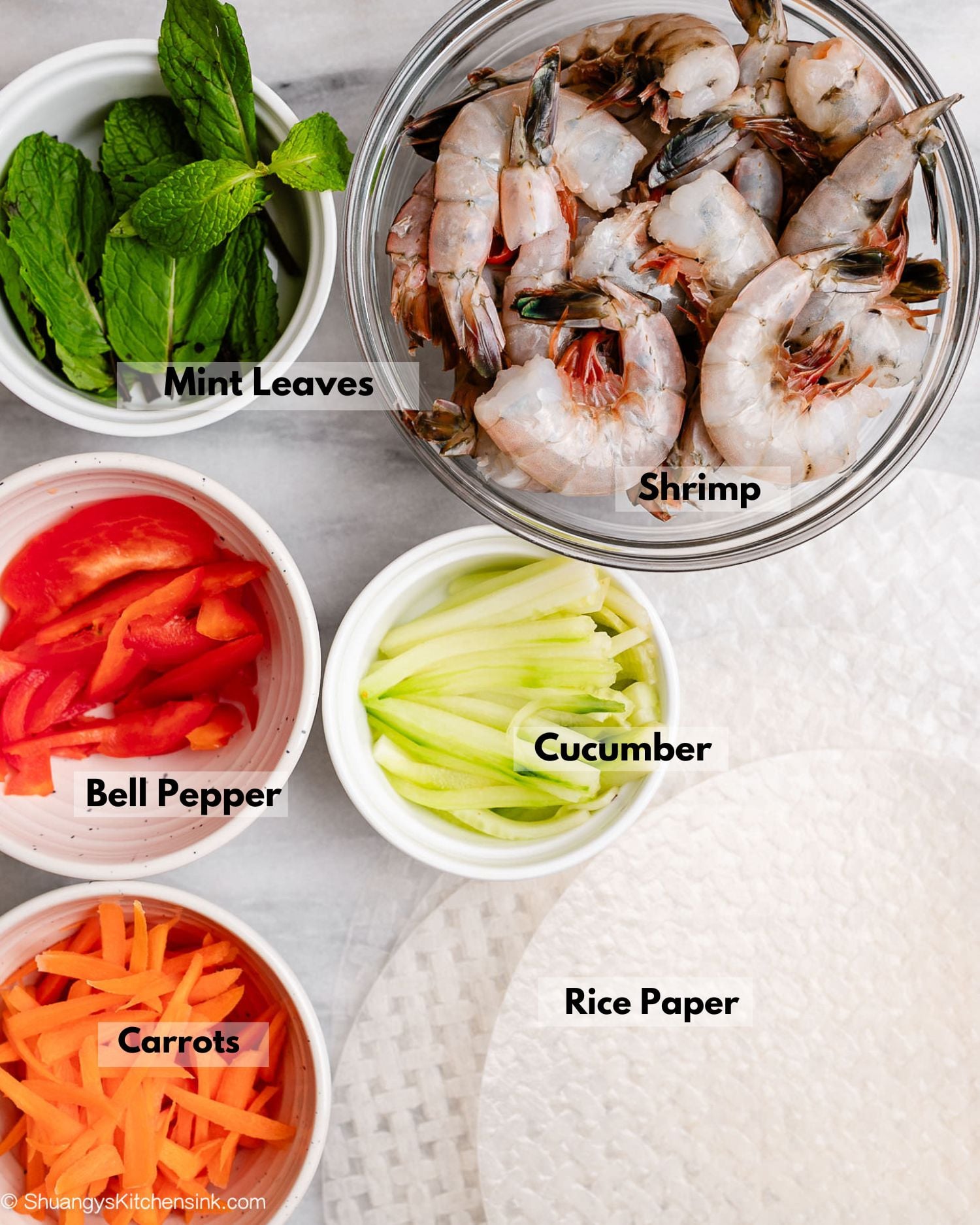 Ingredients for fresh shrimp spring rolls. On a board there are raw shrimps, fresh mint leaves, cucumbers, bell peppers, carrots and rice paper.