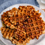 A plate of apple pie waffle pops with cinnamon sugar on top and maple syrup drizzled over.
