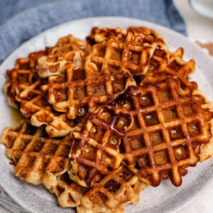 A plate of apple pie waffle pops with cinnamon sugar on top and maple syrup drizzled over.