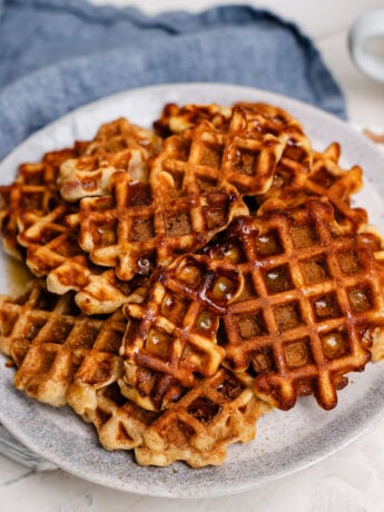 A plate of apple pie waffle pops with cinnamon sugar on top and maple syrup drizzled over.