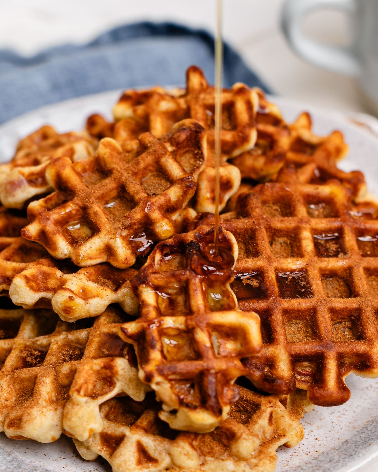 Apple pie waffle bites sprinkled with cinnamon sugar and drizzled with maple syrup on a plate.