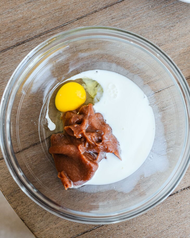 Apple butter, an egg, and milk in a glass mixing bowl