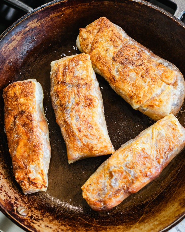 Apple pie spring rolls browning in a skillet until golden and crispy