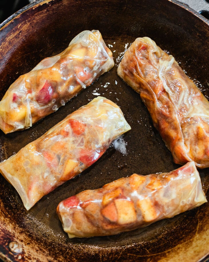 Apple pie spring rolls in a skillet with space between each one