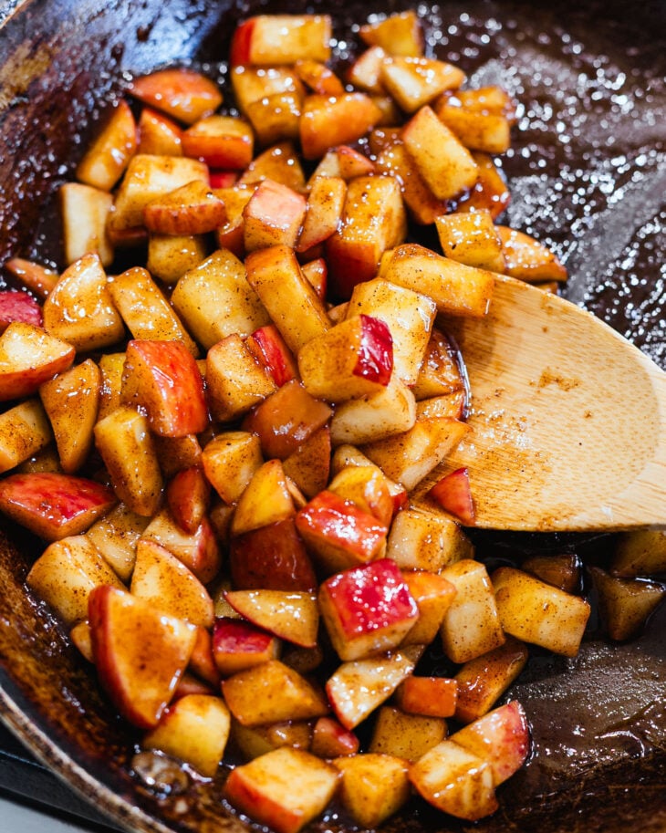 Chopped apples cooking in a skillet with coconut oil, apple pie spice, and maple syrup