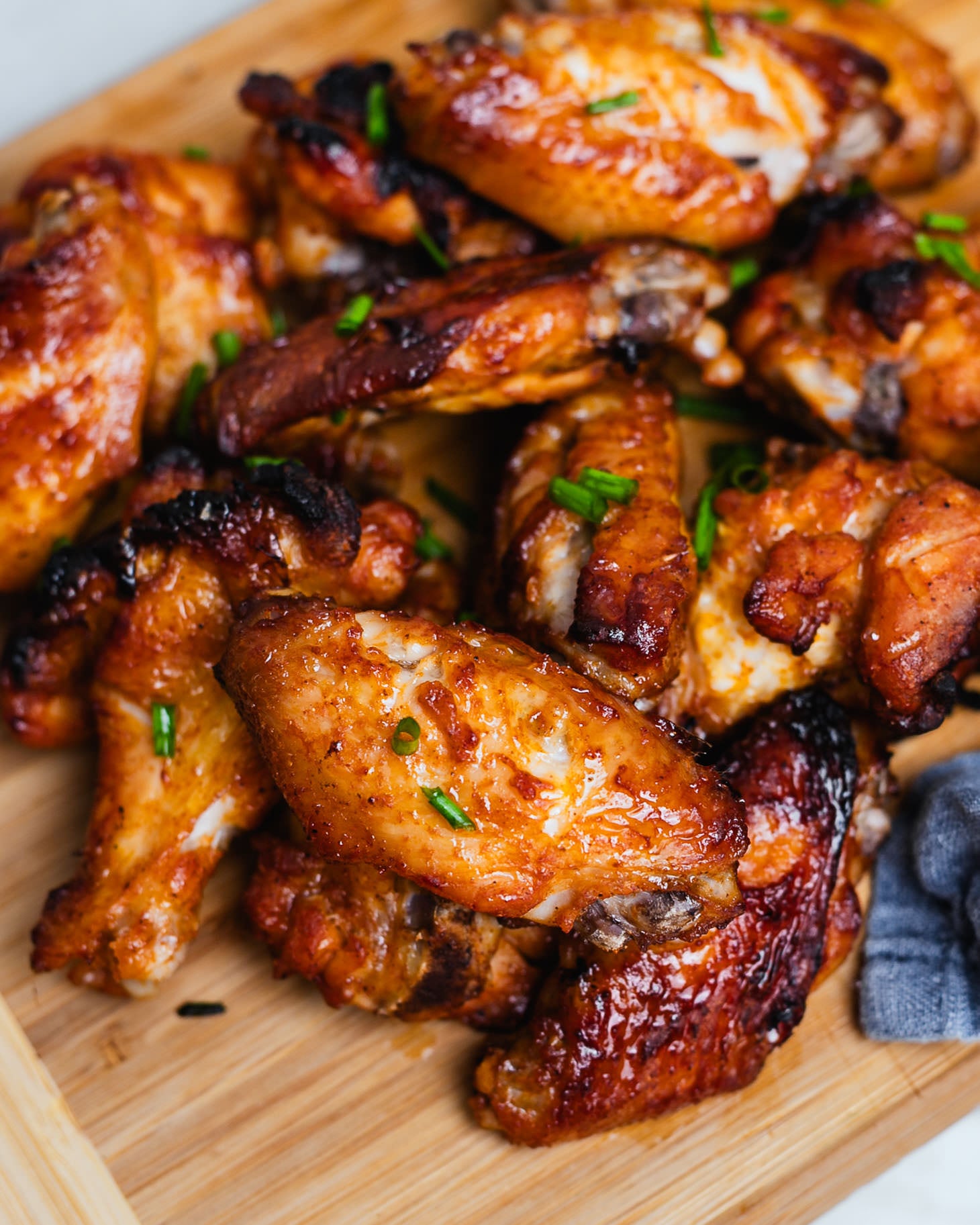 Crispy honey soy chicken wings on a wooden board with green onions