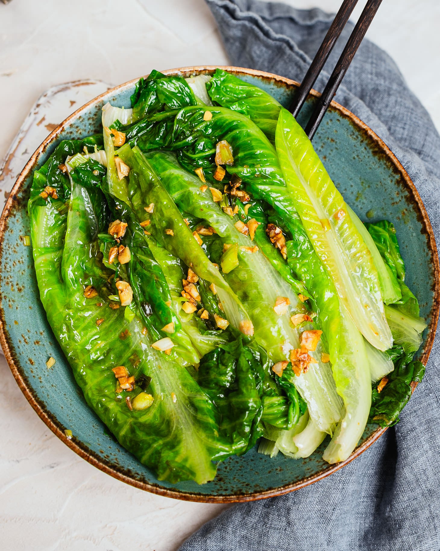 Chinese garlic lettuce on a blue plate topped with golden garlic and green onion, with chopsticks