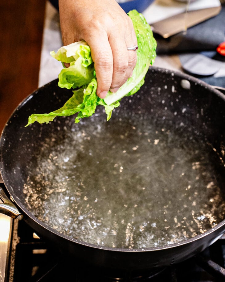 Hand dropping a romaine leaf into boiling water