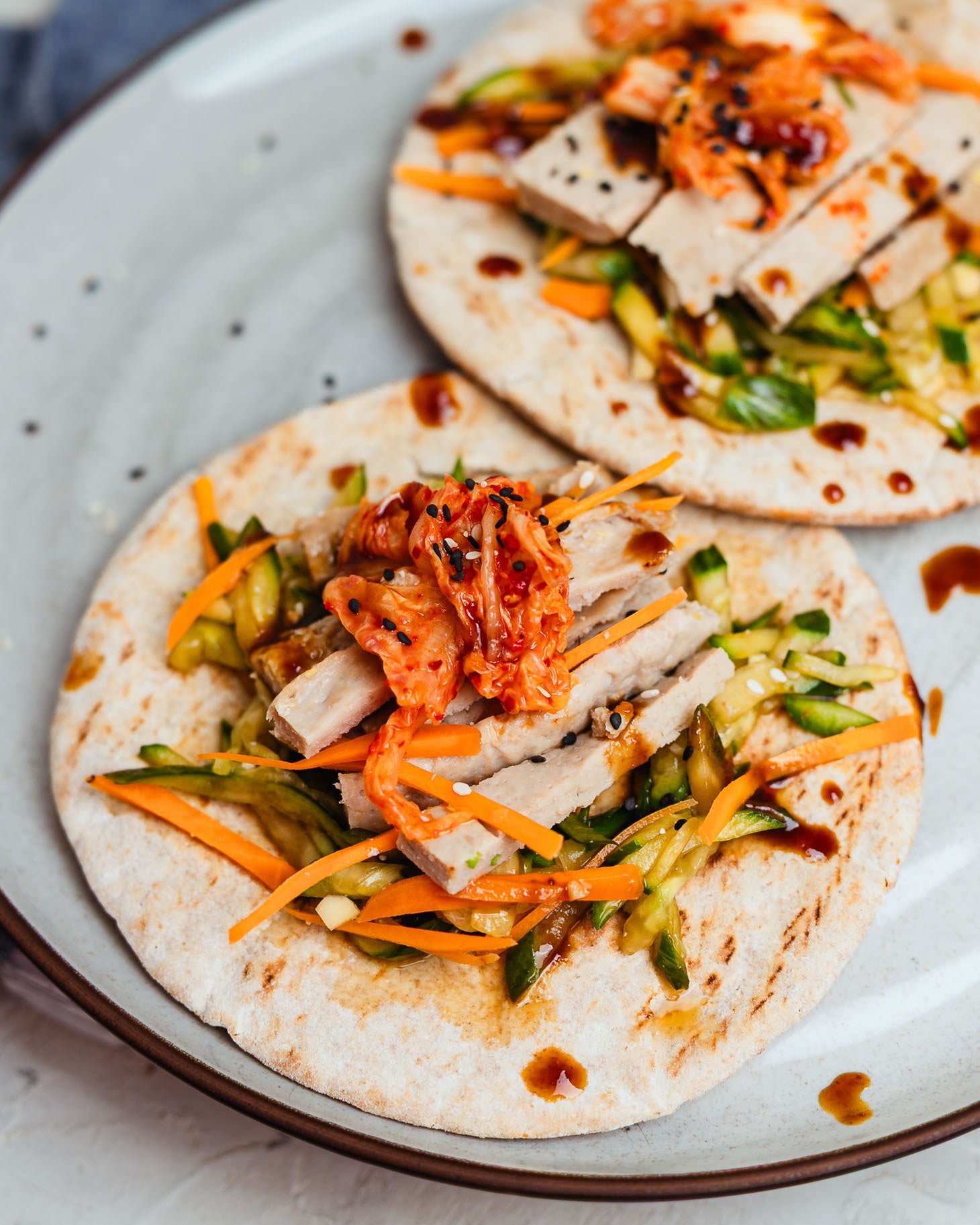 Two dumpling wraps with sliced filling, shredded veggies, and sauce on a plate