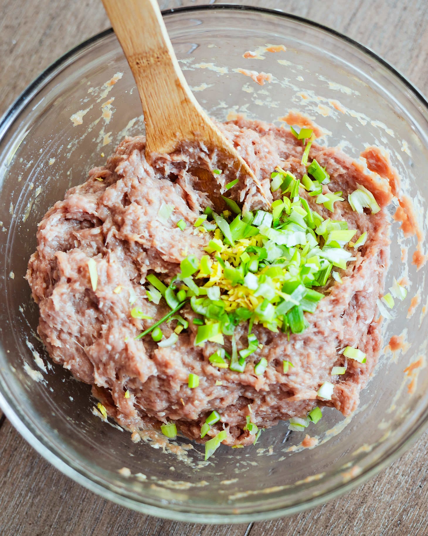 Pork dumpling filling with green onions and ginger in a glass mixing bowl